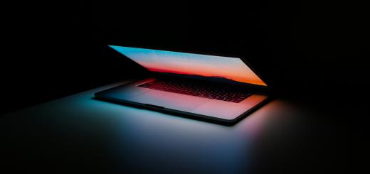 A photo of a laptop in a dark room slightly open, with a sunrise showing on the screen which reflects onto the keyboard