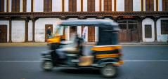 Photo of a motion-blurred autorickshaw driving down a street in India