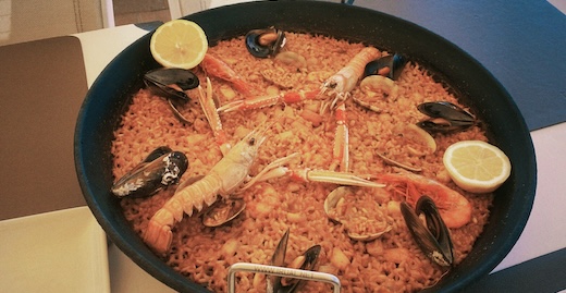 A photo of a paella dish with seafood on the top.