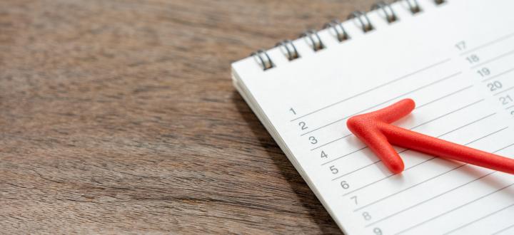 Image of a notebook with a calendar on a wooden table with a red arrow pointing to the dates