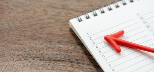 Image of a notebook with a calendar on a wooden table with a red arrow pointing to the dates