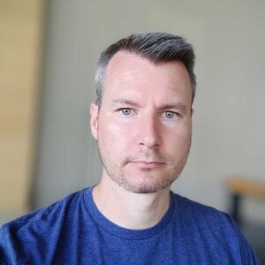 Photo of a white man with short dark hair wearing a blue Mautic tshirt.