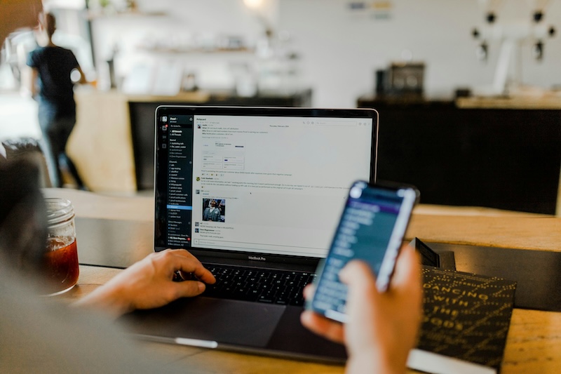 Photo of a person using a laptop and a mobile phone.