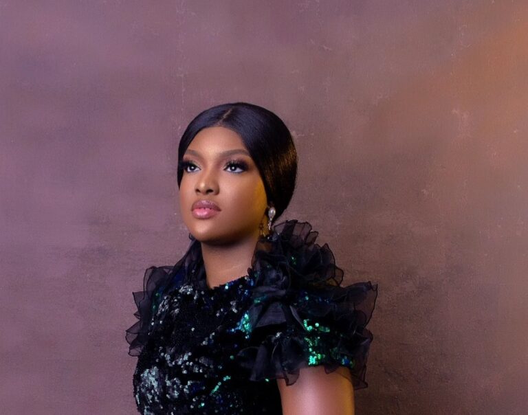 Photo of a black woman with dark hair tied back, wearing a dark coloured top with sequins and lace.