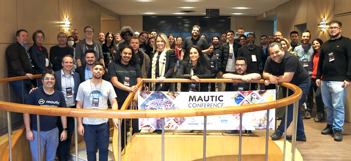 Photo of a diverse group of people around a stair well with a Mautic Conference South America banner on the stairs.