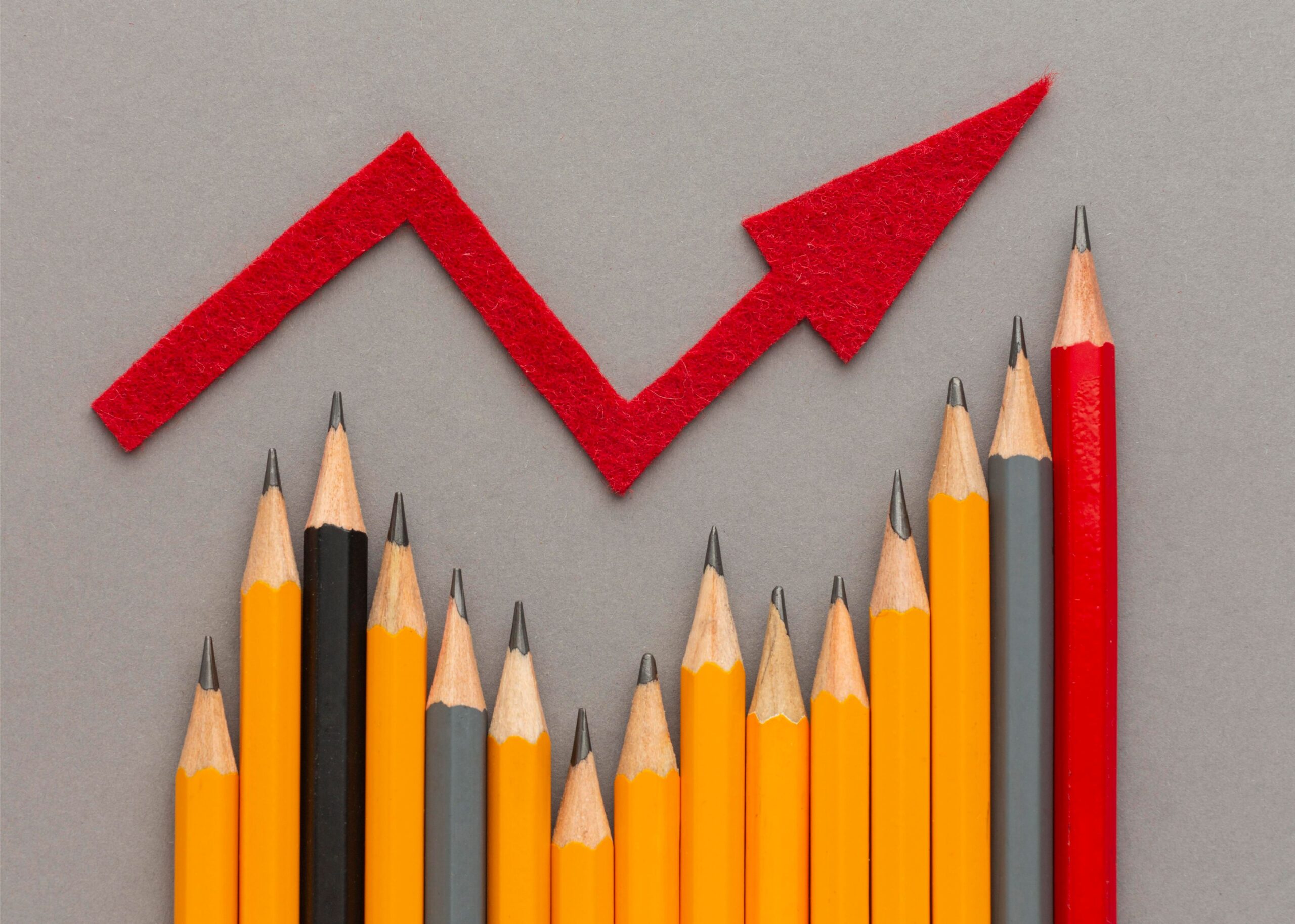 A photo of some differently coloured pencils indicating a bar graph, and a red arrow above which indicates growth in an up and right direction.