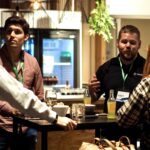 Photo of four people standing around a table at a conference talking.