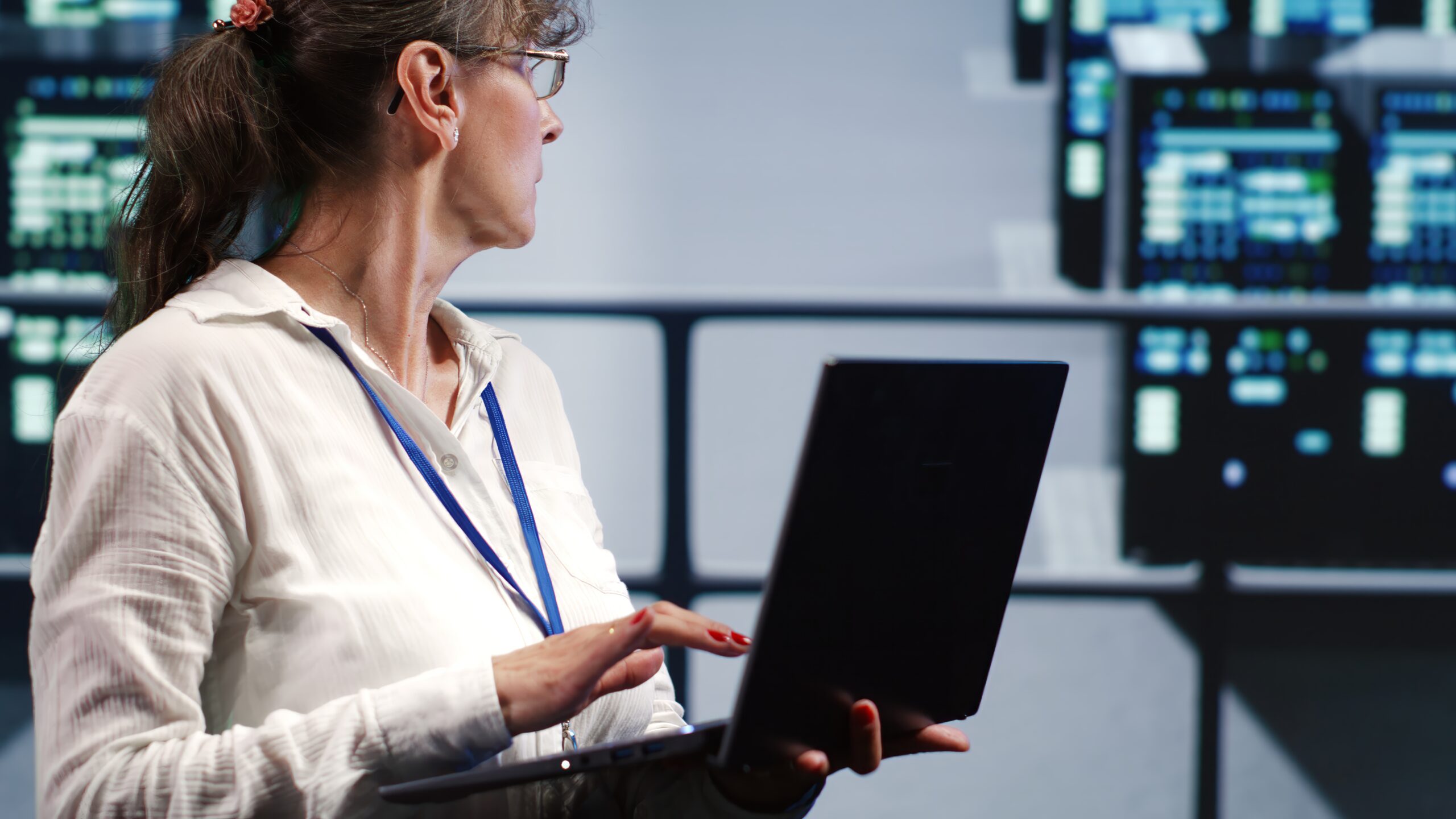 A woman holding a laptop looking back towards a server farm.