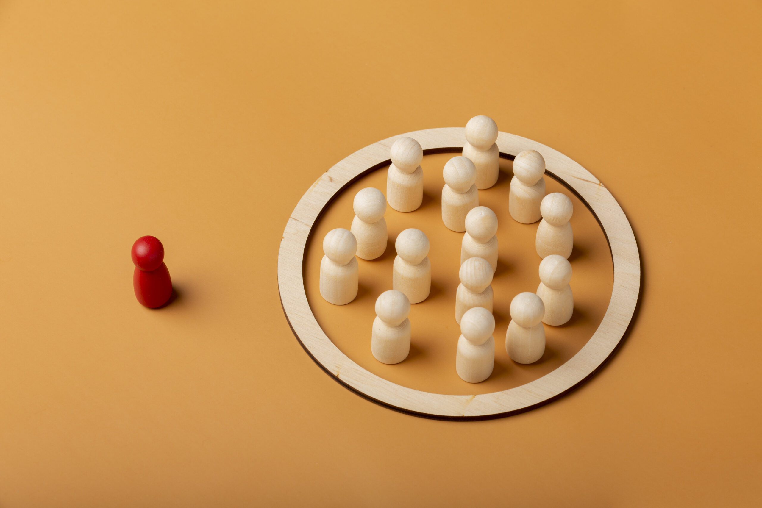 Photo on a yellow background of a single red chess piece on the left, and a white circle which encloses lots of white chess pieces grouped together.