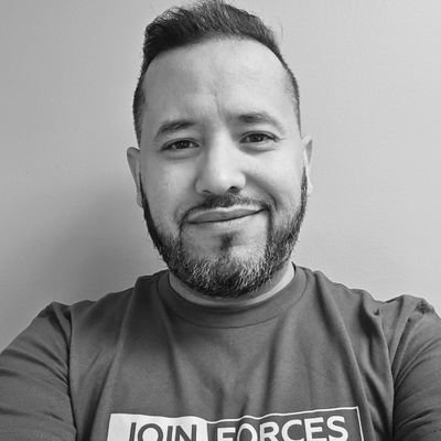 Photo of a man with short hair and a beard, goatee and moustache wearing a tshirt which says 'join forces' on it.