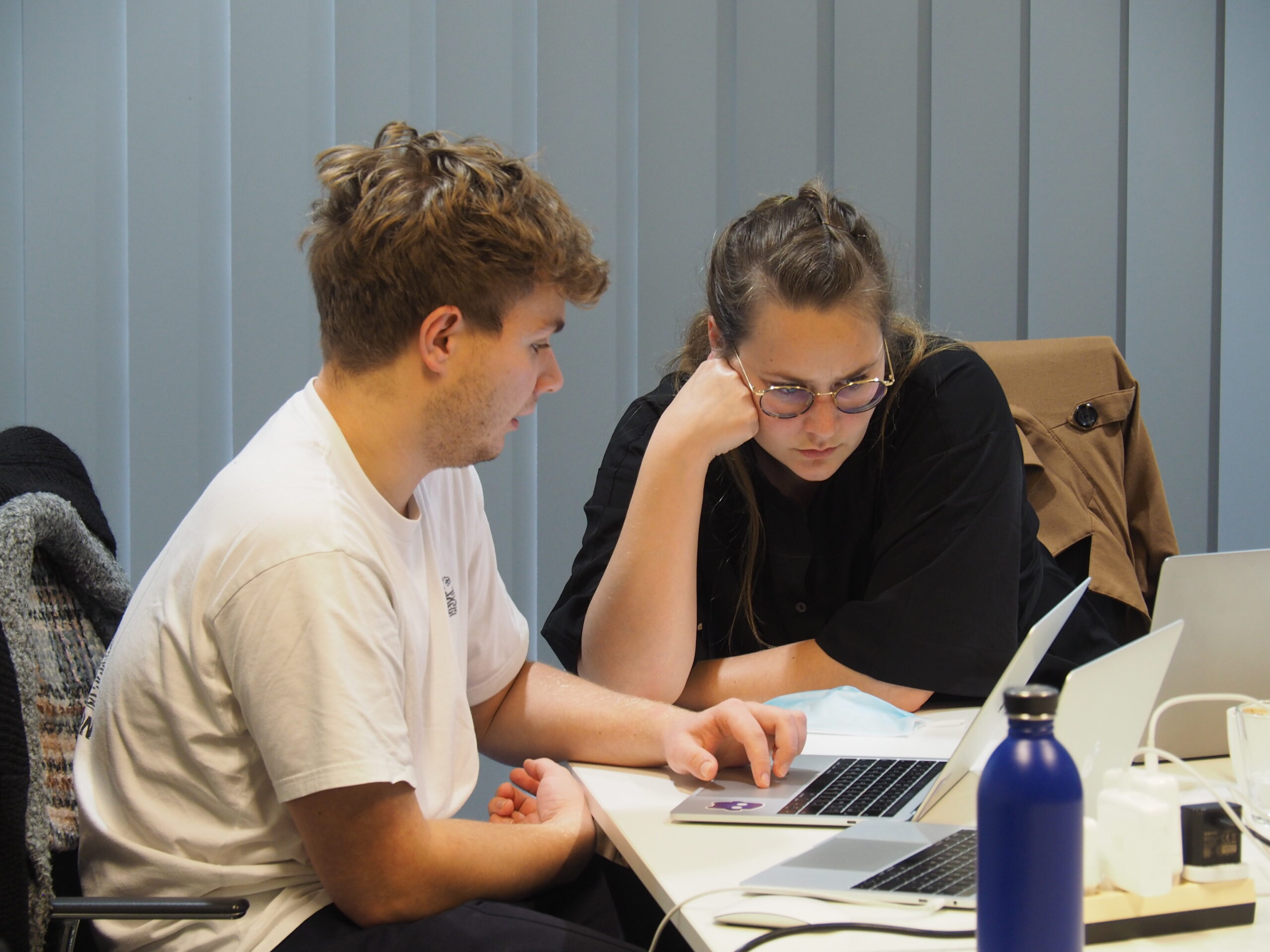 Photo of two people sitting at a desk, a man and a woman, looking at a laptop.