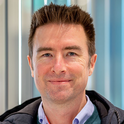 Photo of sebastian selch, a white man with short spikey dark hair smiling at the camera wearing a pale coloured short and a jacket.