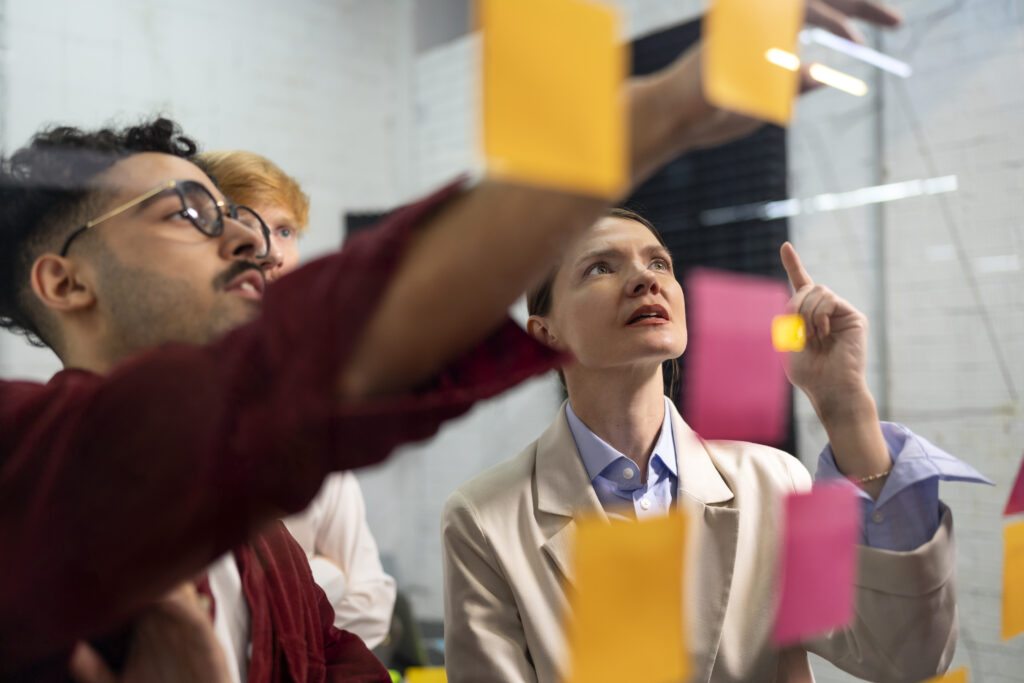 Photo of a diverse group of people looking at sticky notes on a glass wall.