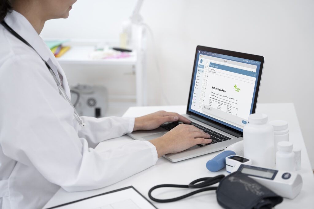 Photo of a doctor at a computer screen typing up a medical history. There's a stethoscope and other medical equipment on the desk beside her.