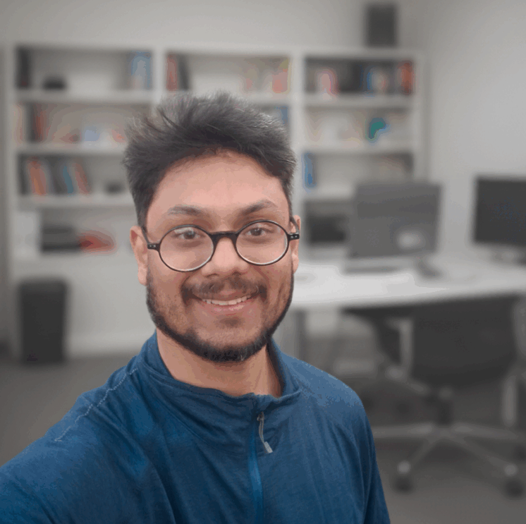 Photo of Tejas Shah, he's an Indian man with short spikey black hair, a moustache and a beard wearing dark rimmed glasses and a blue coloured jumper.