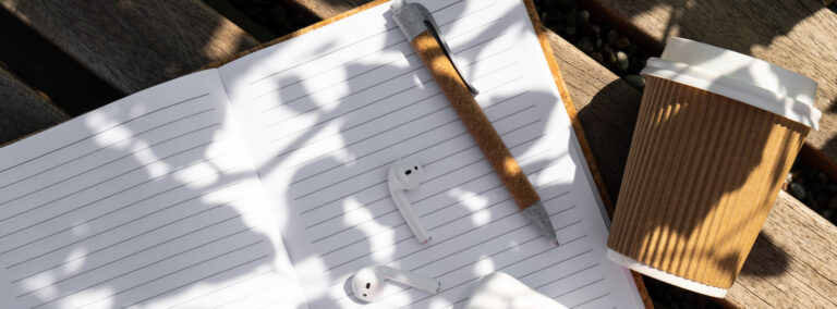 Take away coffee in craft recycling paper cup with paper notebook with wireless headphones.