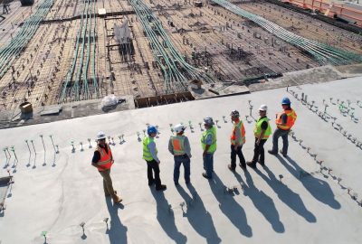 Photo of a building site with people standing on the foundations wearing high vis jackets and hard hats.