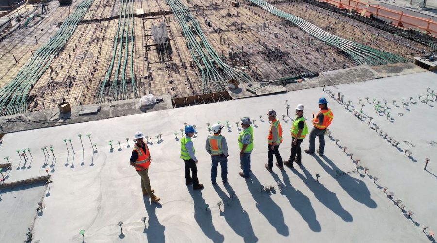 Photo of a building site with people standing on the foundations wearing high vis jackets and hard hats.