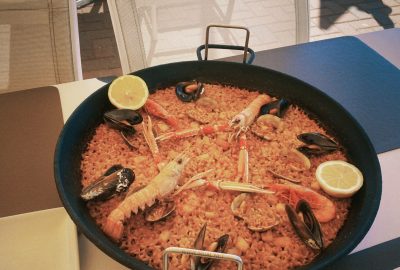 A photo of a paella dish with shrimps and lemons on top of the rice.