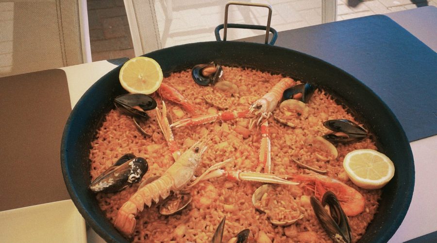 A photo of a paella dish with shrimps and lemons on top of the rice.